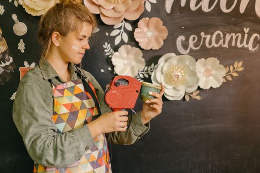 A young woman in an apron labeling a handcrafted ceramic cup in a creative workspace.
