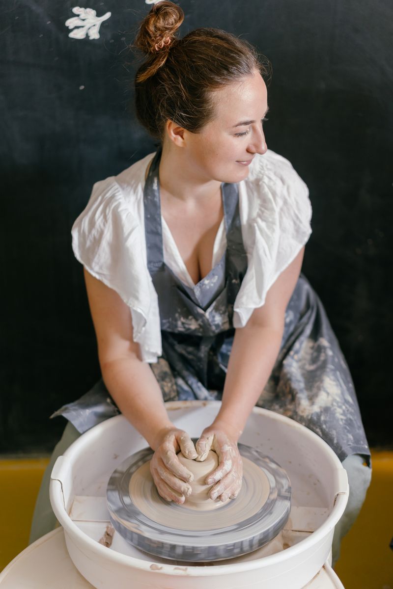 A potter in a grey apron shaping a lump of clay on a spinning wheel