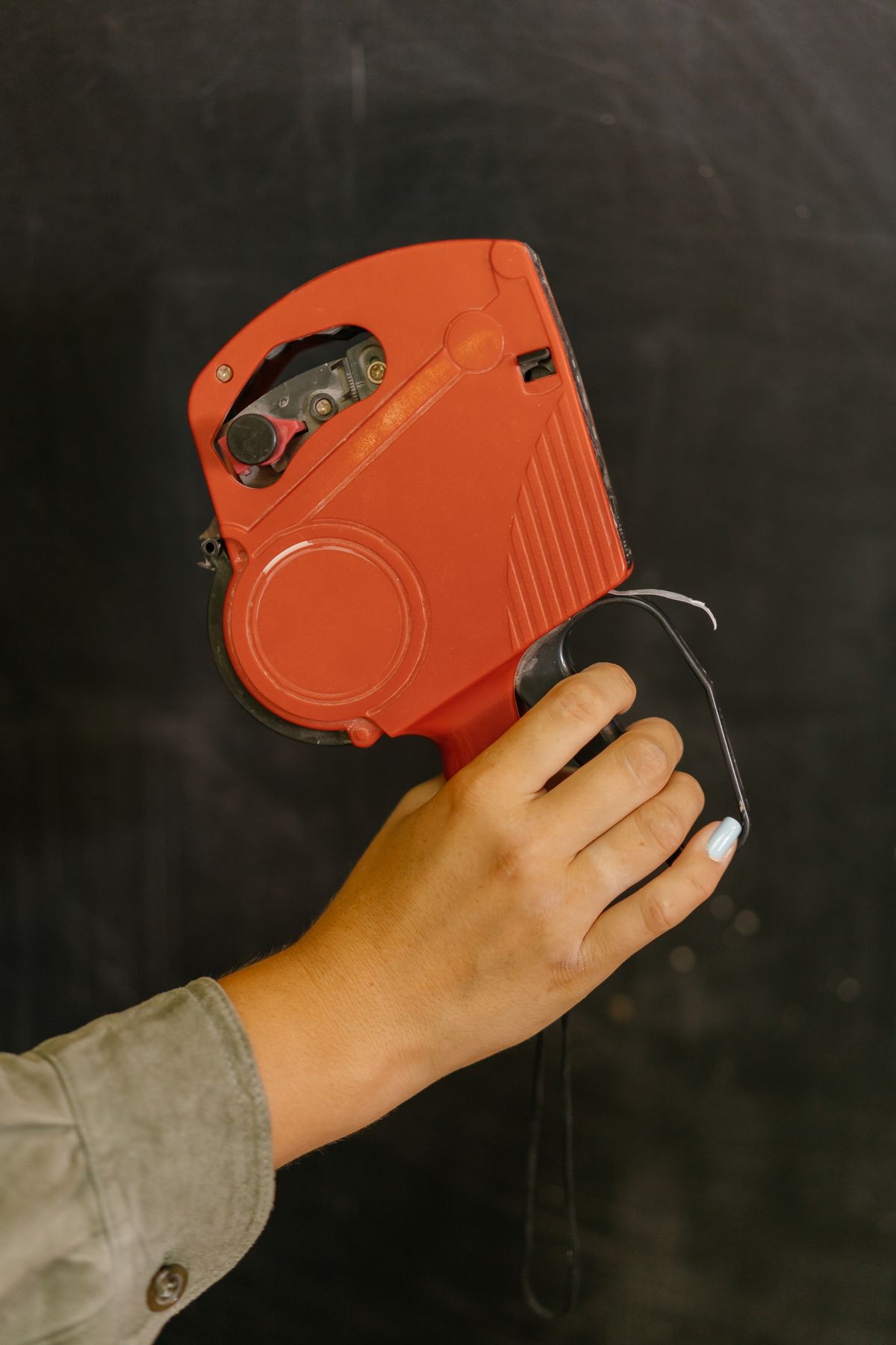 A hand holding a red price tag gun used for labeling