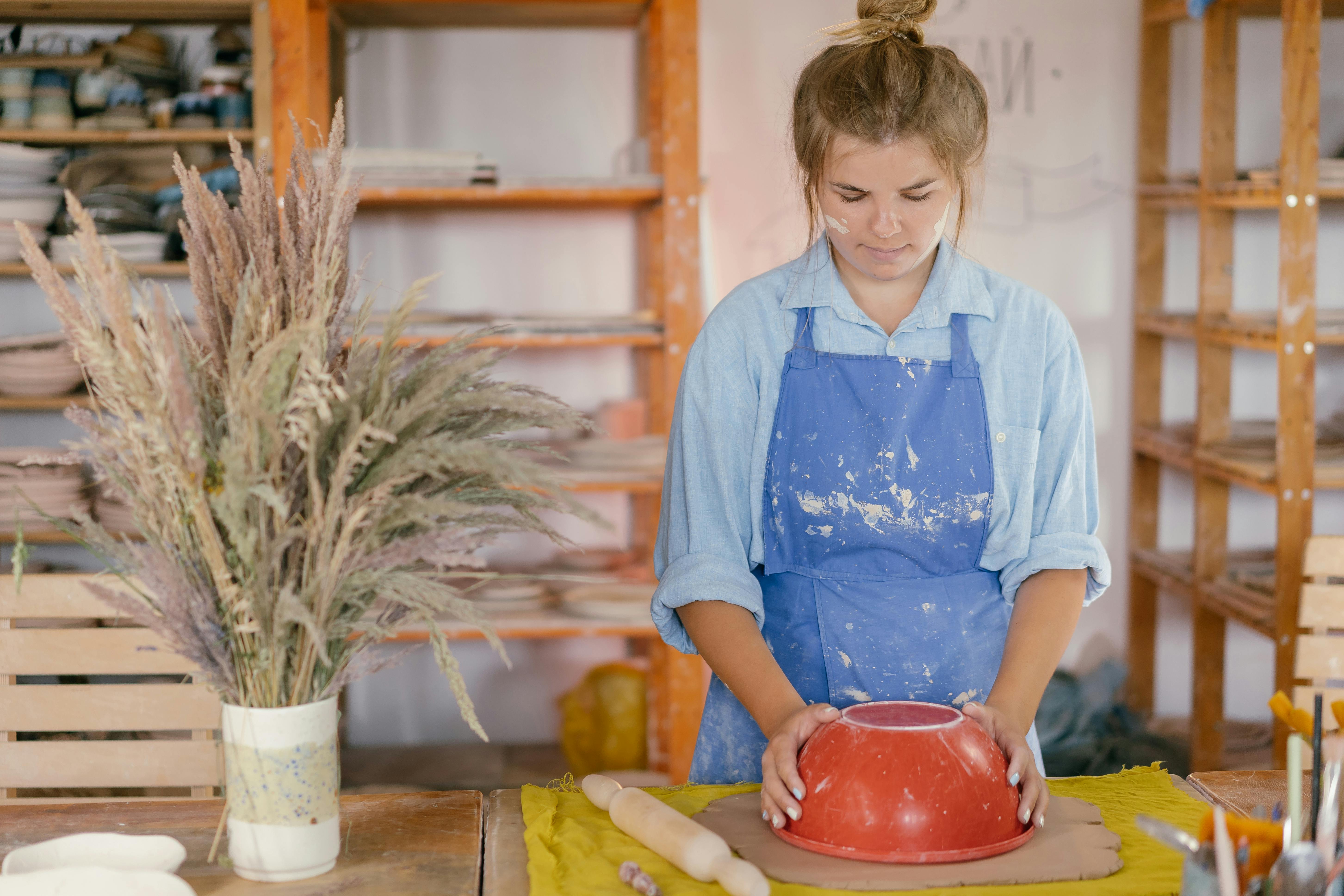 woman putting red bowl on clay in workshop