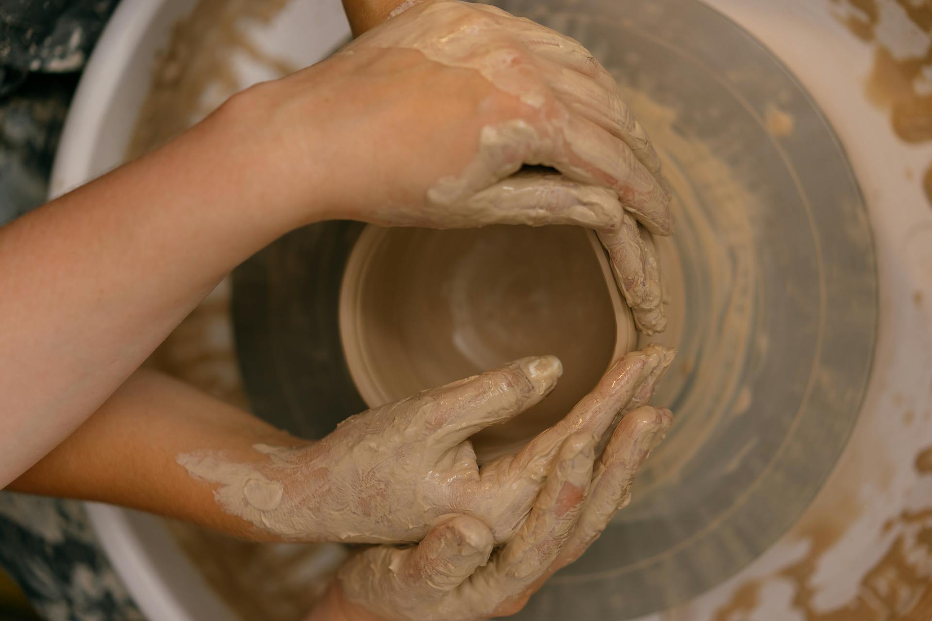 Muddy Hands Shaping Clay on a Potter's Wheel