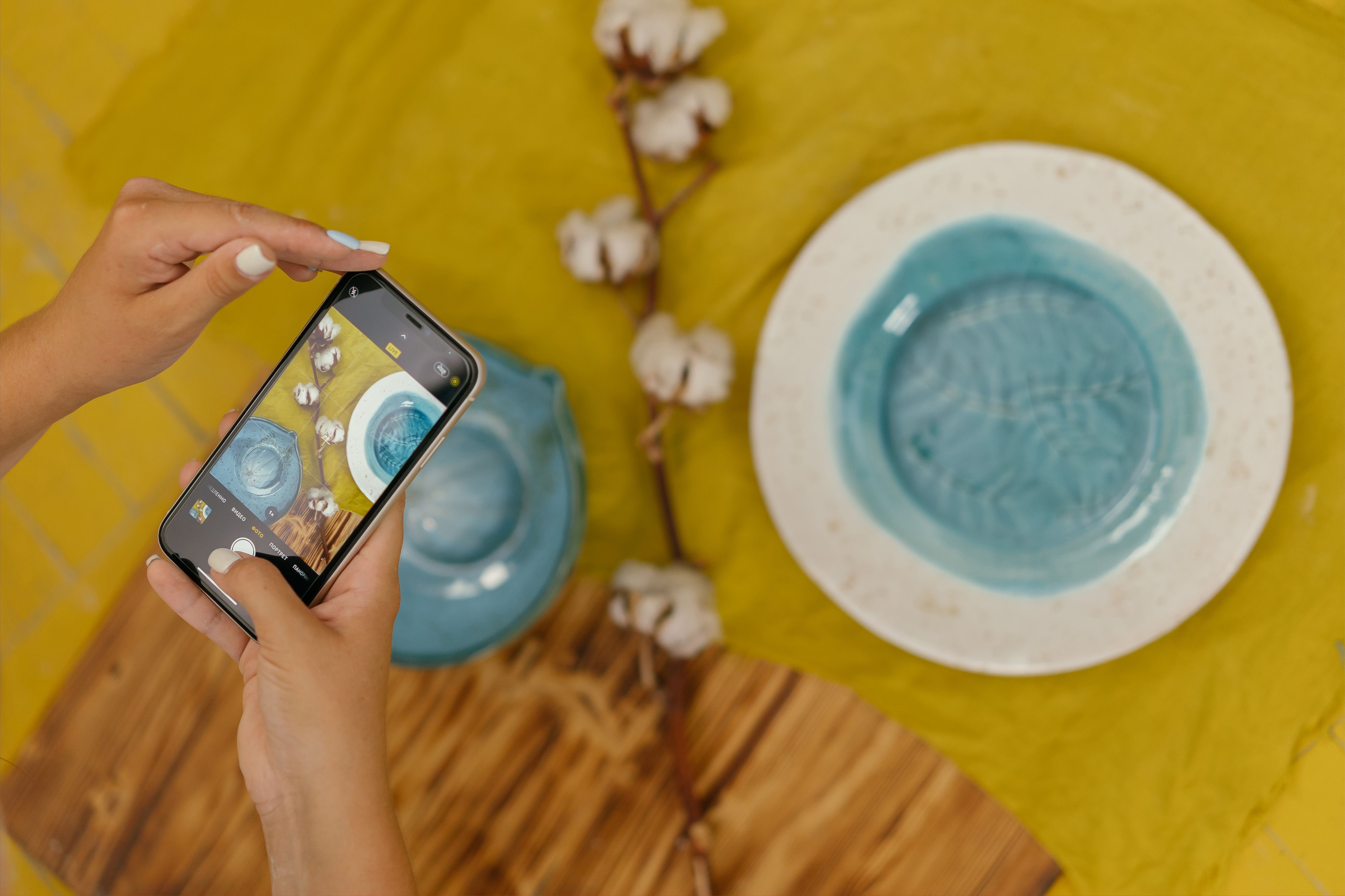 Overhead view of handmade ceramics being photographed with a smartphone, showcasing craftsmanship