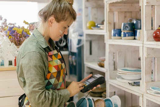 Caucasian woman using a POS machine in a ceramic store, showcasing modern retail technology.