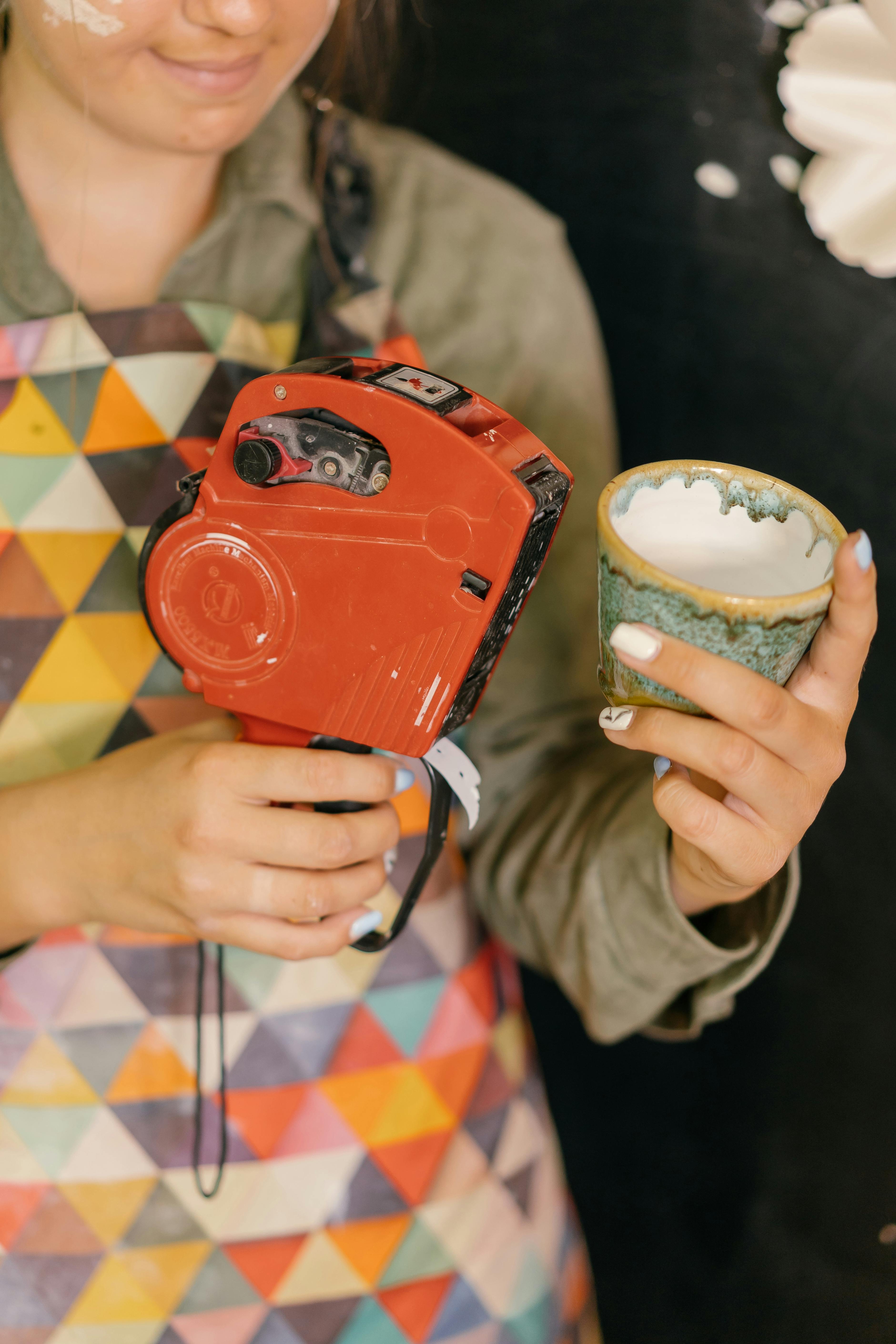 A woman holds a handmade ceramic cup and a price tag gun, ready for selling.