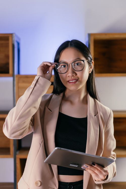 Free Portrait of a confident businesswoman adjusting her glasses while holding a tablet indoors. Stock Photo