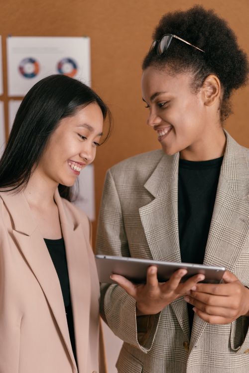 Free Two businesswomen in blazers share a moment of collaboration and happiness indoors. Stock Photo