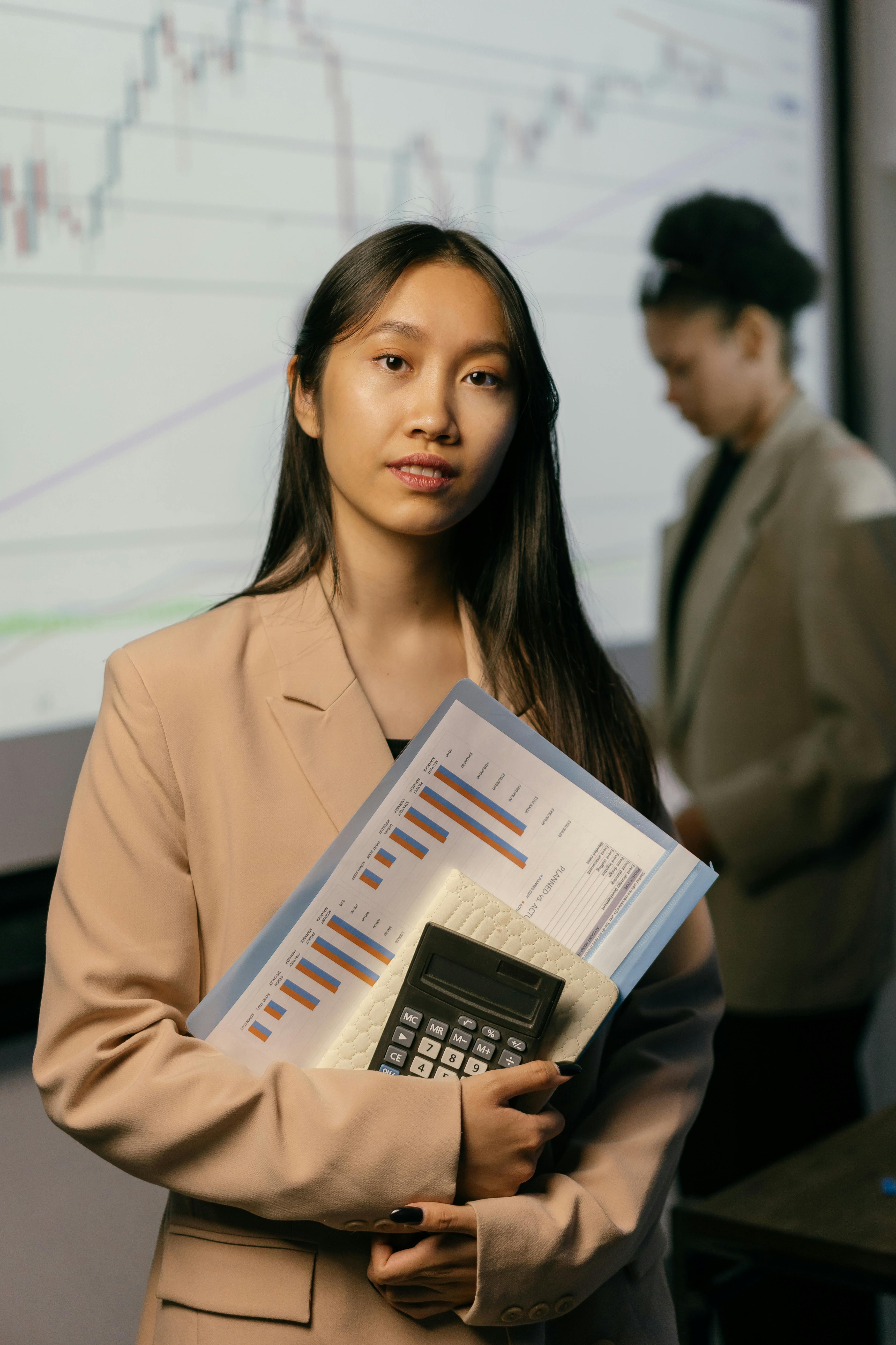 woman in a beige blazer holding a calculator and paper