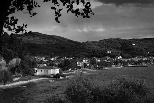 Grayscale Photo of Riverside Town Near Hills