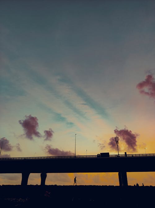 Silhouette of Person Walking Under the Bridge During Golden Hour 