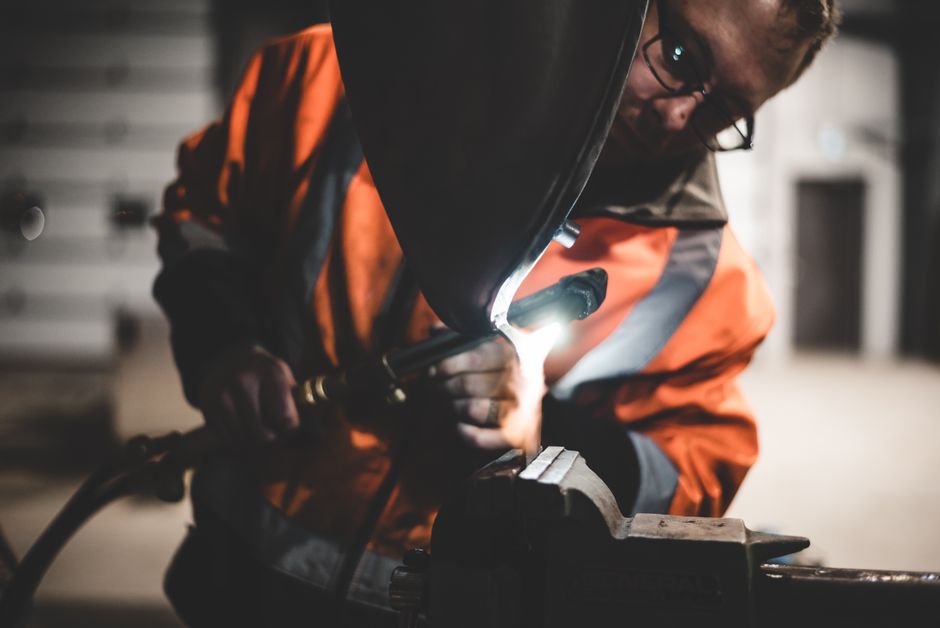 Close-up of a welder wearing safety gear working on metal equipment in an industrial setting.
