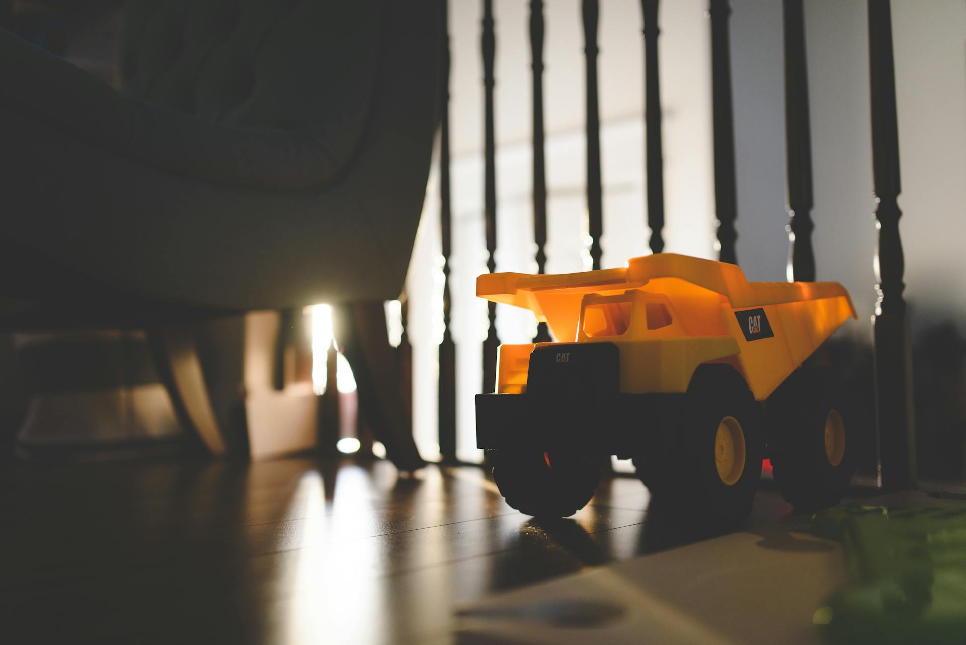 A yellow toy dump truck backlit by sunlight, casting shadows on a wooden floor indoors.