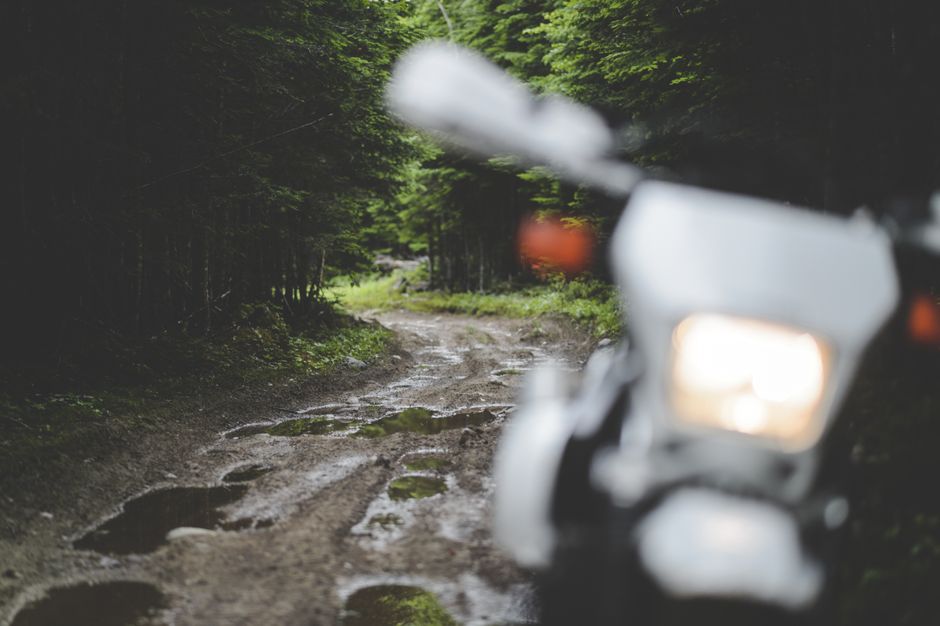 A motorbike parked on a dirt road amidst a lush forest with puddles, suggesting recent rain.