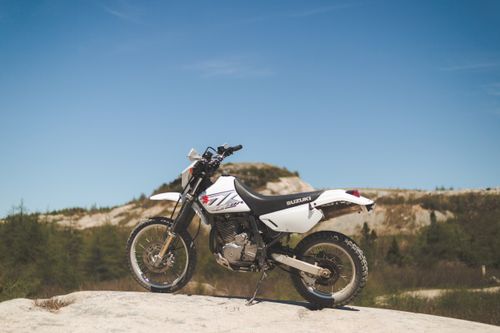 Free A powerful Suzuki dirt bike perched on a rocky cliff in a sunny outdoor landscape. Stock Photo
