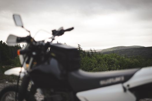 Blurred motorcycle in the foreground with scenic hills and trees in the background.