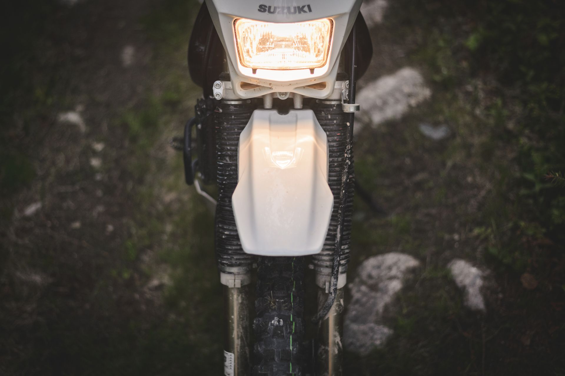 Front view of a Suzuki motorcycle headlight, illuminating a rugged dirt path, perfect for adventure enthusiasts.