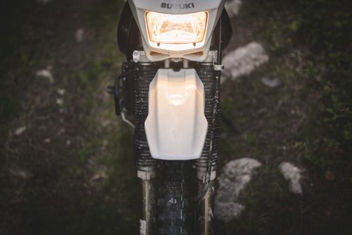 Free Front view of a Suzuki motorcycle headlight, illuminating a rugged dirt path, perfect for adventure enthusiasts. Stock Photo