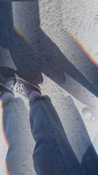 Abstract view of a person wearing Converse sneakers and denim pants on a sunlit street with shadow play.