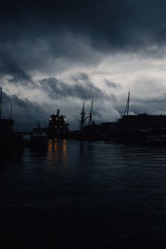 Harbour Nights key art — dark moody harbour under a dramatic cloudscape, photo by Adrien Olichon on Pexels