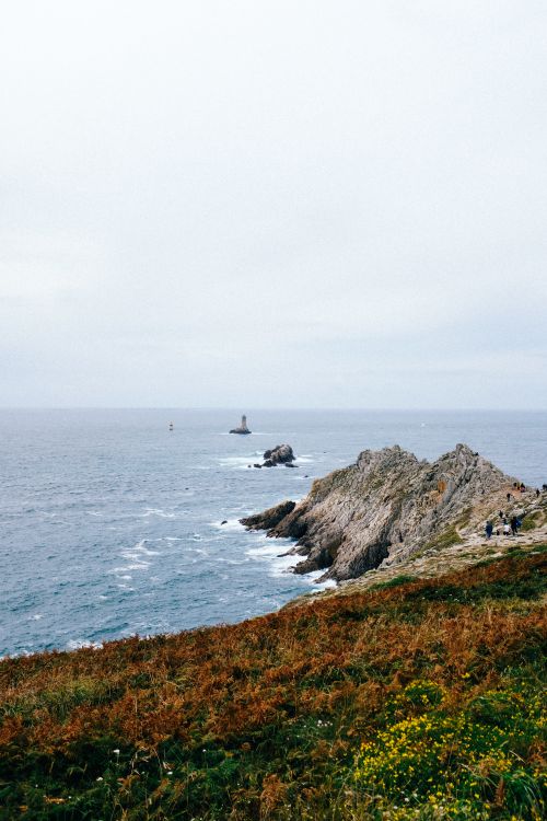 Free A stunning view of a rugged coastline with a distant lighthouse on a calm day. Stock Photo