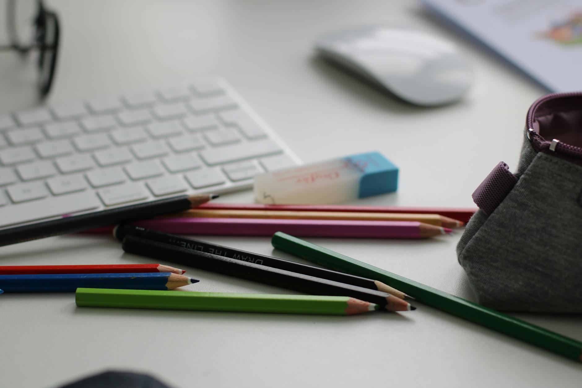 Color pencils and office supplies scattered on a white desk with keyboard and mouse.