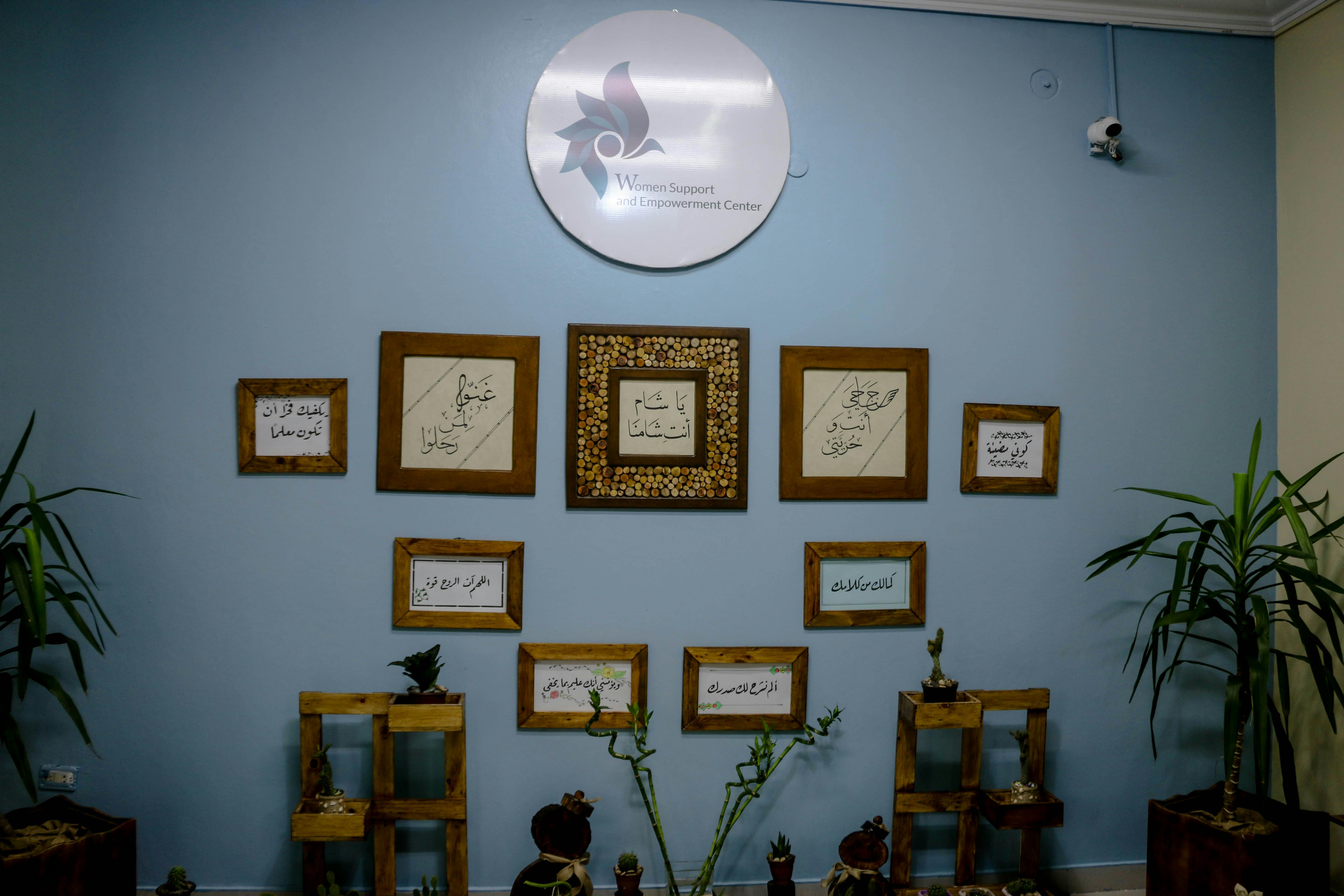 Wall decorations in a Women Support and Empowerment Center featuring framed calligraphy and plants.