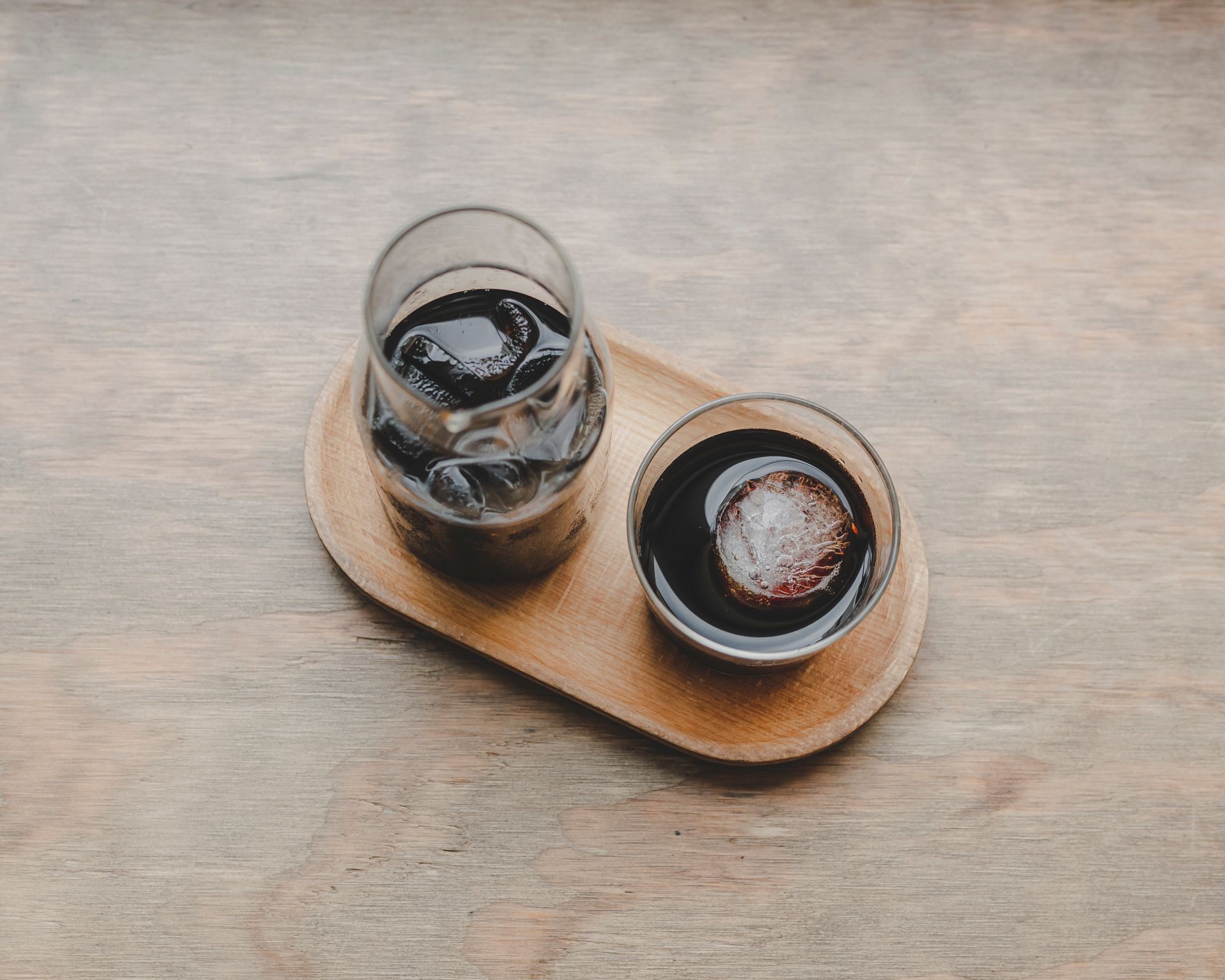 Aesthetic shot of iced coffee beverages on a wooden tray, showcasing a simple and relaxing setup.