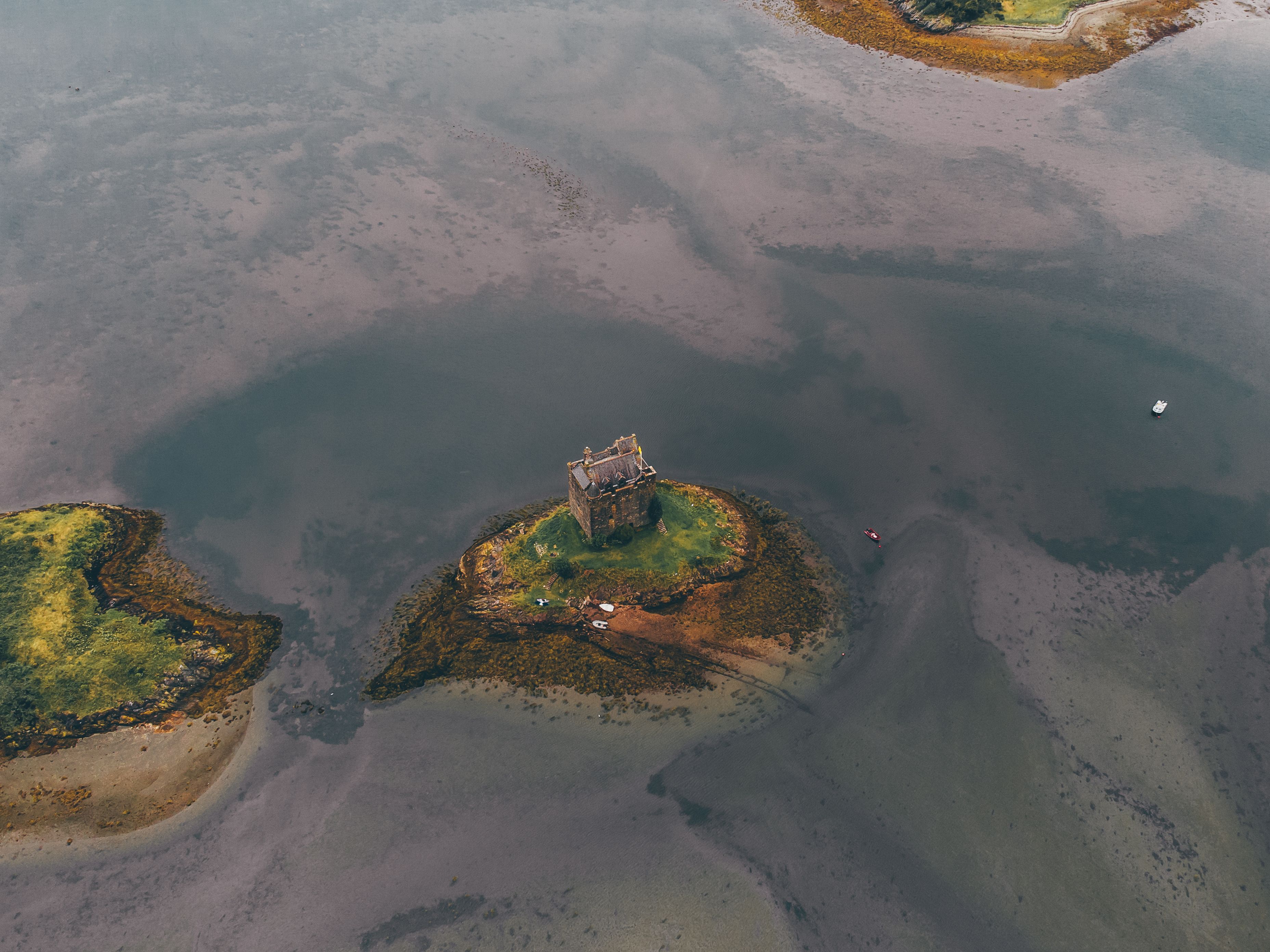 Captivating aerial shot of Castle Stalker amidst serene waters in Scotland.