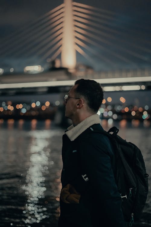 A Man in Black Jacket Standing Near Body of Water during Night