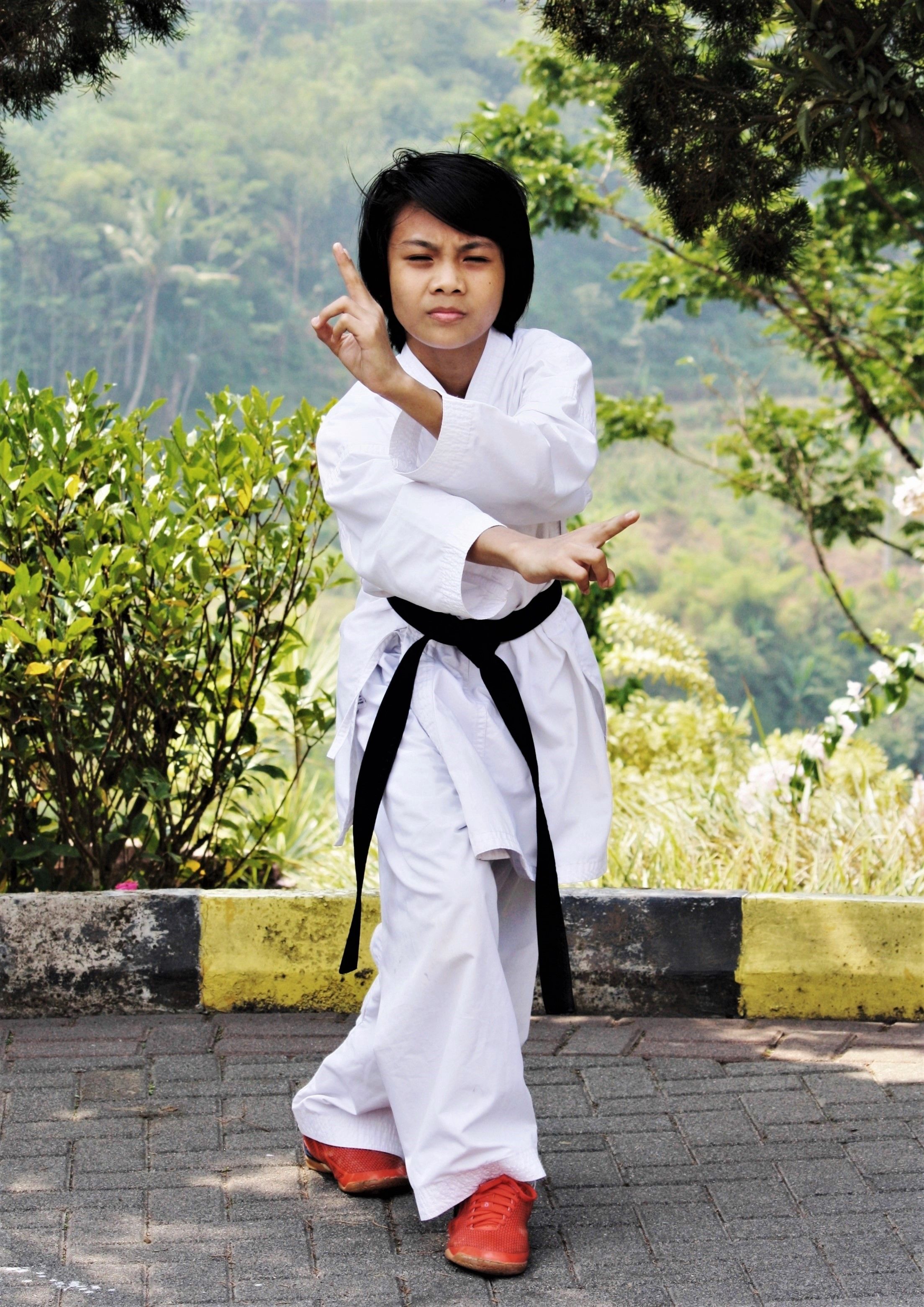 Child practicing martial arts pose outdoors in a white uniform and black belt.