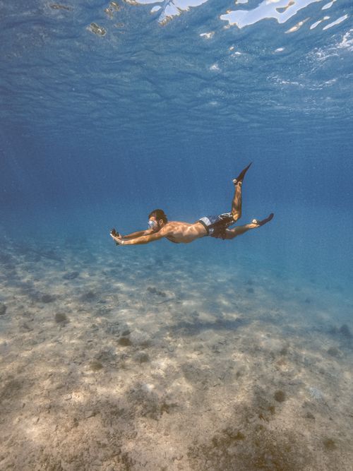 Free A man free diving underwater over a rocky sea floor in Arraial do Cabo, Brazil. Stock Photo