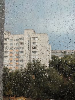Raindrops on a windowpane with a blurred cityscape in the background.