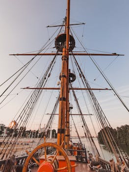 View of a vintage sailboat's mast in a harbor at sunset, invoking a sense of maritime adventure.