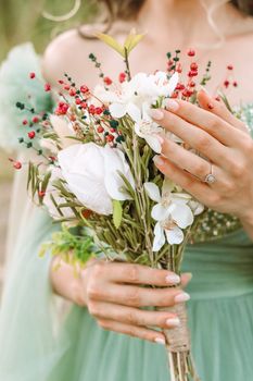 Close-up of an elegant green dress and hands holding a delicate floral bouquet.