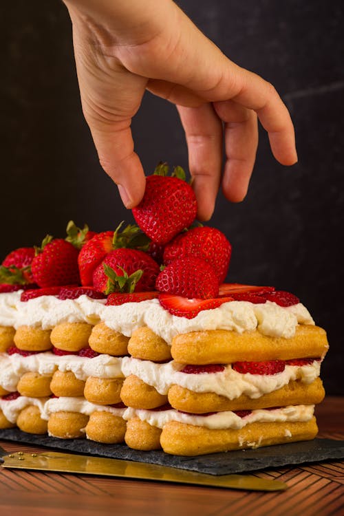 Hand Holding Strawberry on Sponge Cake