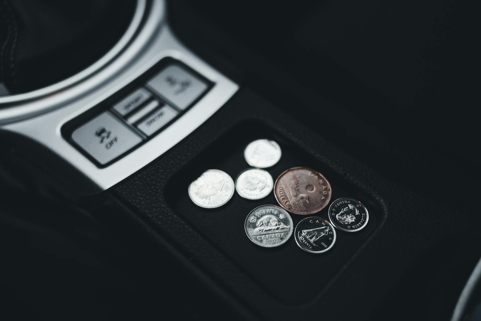 Close-up view of coins neatly placed in a car's console compartment, emphasizing currency and money themes.