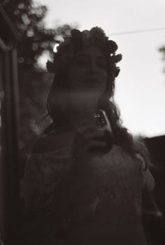 A woman in silhouette holding a drink, wearing a floral crown, captured in atmospheric grayscale.
