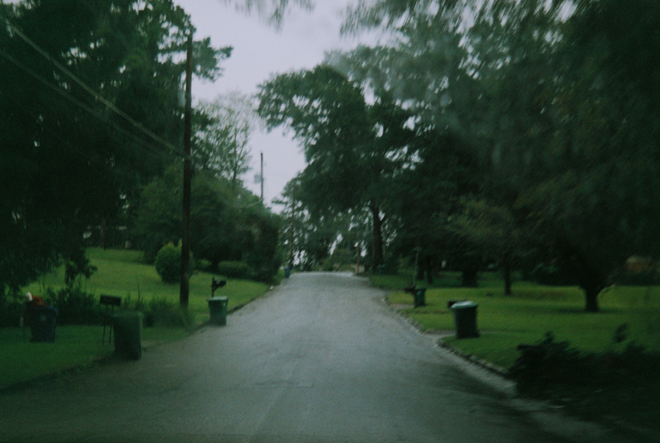 A tranquil and blurred view of a quiet neighborhood street bordered by lush green trees and pathways.