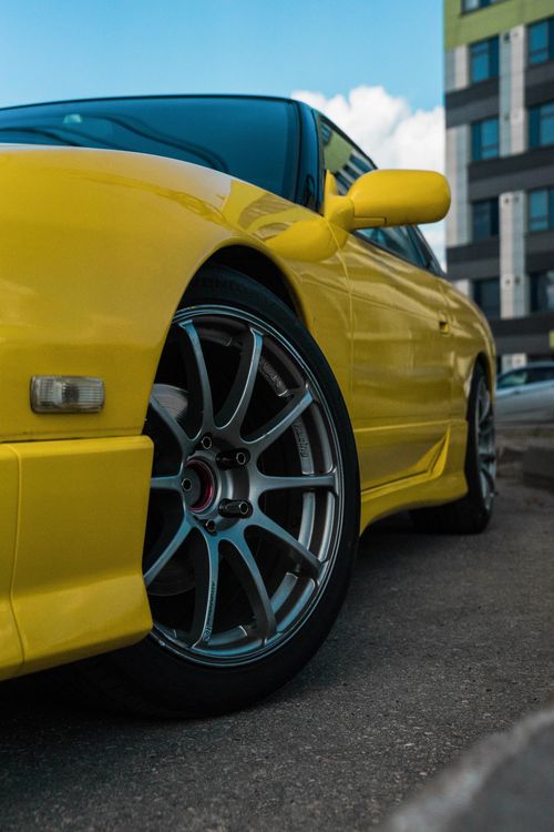 Free Detailed view of a yellow Nissan 180SX parked against a cityscape backdrop. Stock Photo