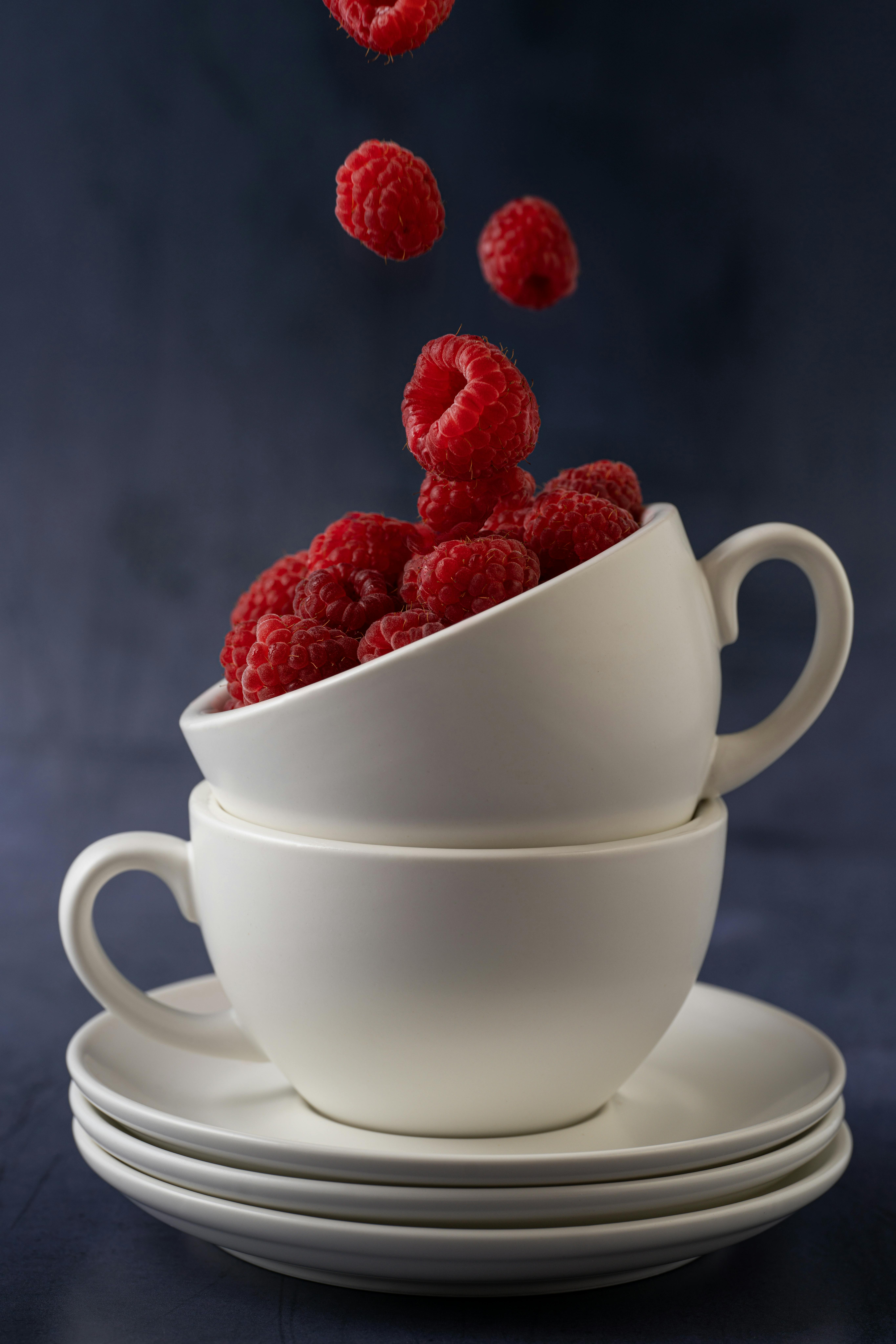 Vibrant ripe raspberries falling into stacked ceramic cups, studio shot.