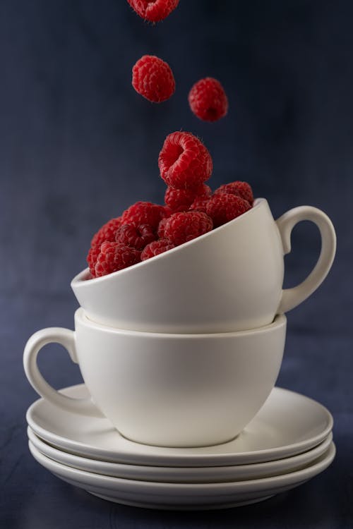 Red Raspberries Falling in a White Ceramic Cup