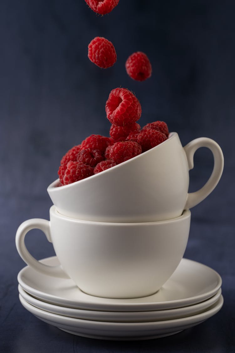 Red Raspberries Falling In A White Ceramic Cup