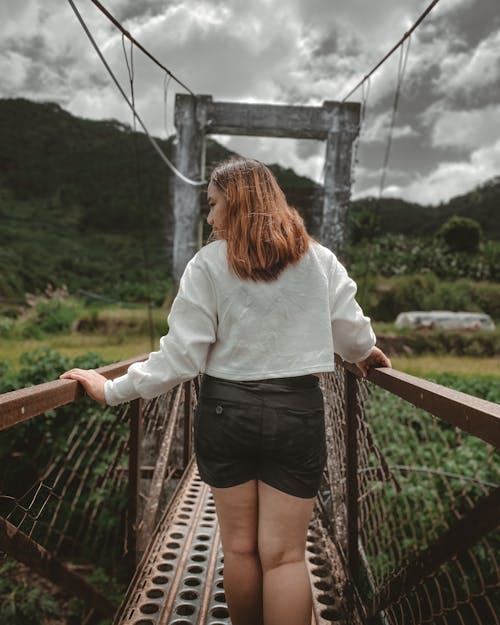 Back View of a Woman in a White Long Sleeve Shirt Walking on a Footbridge