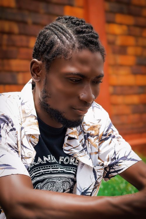 Free Portrait of a young black man with braided hair, smiling outdoors against a brick wall background. Stock Photo