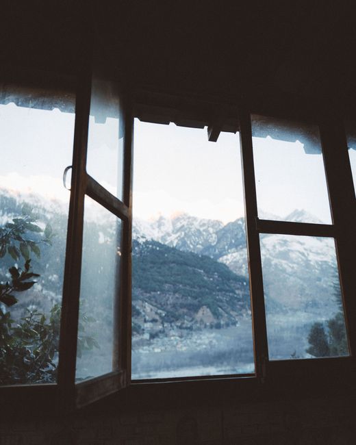 Breathtaking snowy mountain view from a wooden window in Manali, India, showcasing natural beauty.
