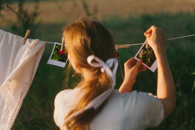 A Person Hanging Polaroid Photographs On A Clothesline