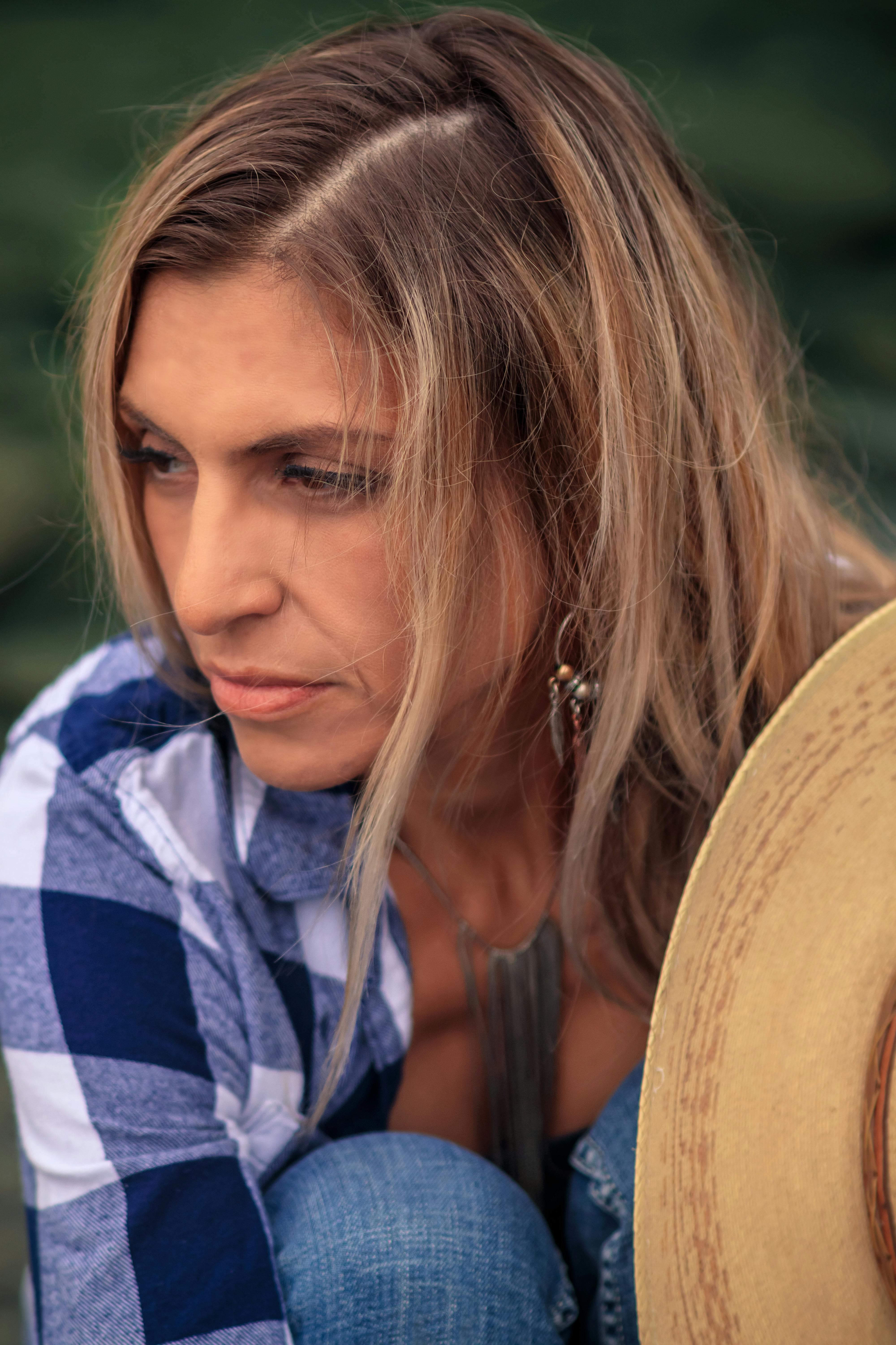 Close-up of a woman in plaid shirt holding a hat and gazing thoughtfully.