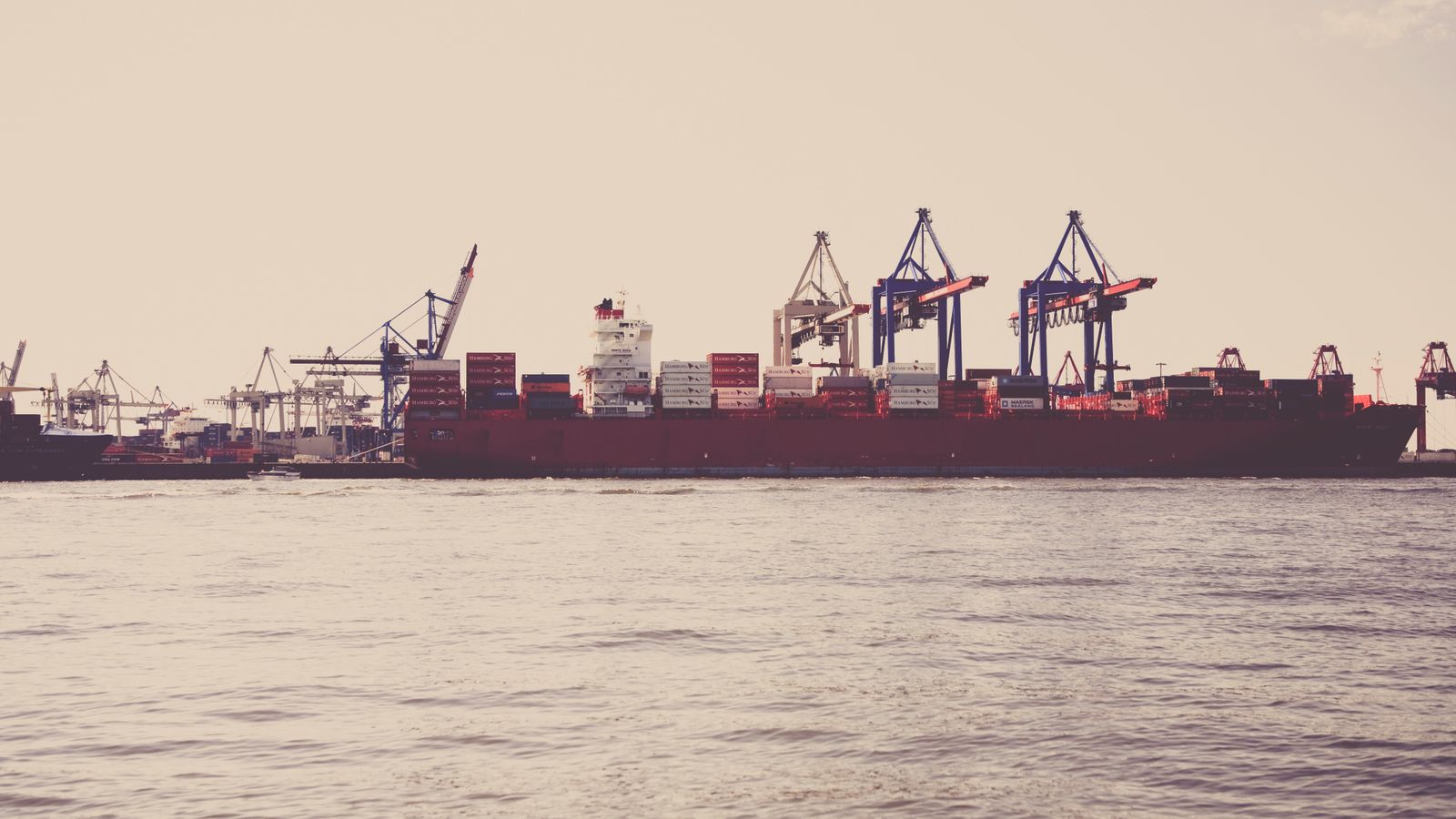 A cargo ship loaded with containers docked at a seaport under clear skies.