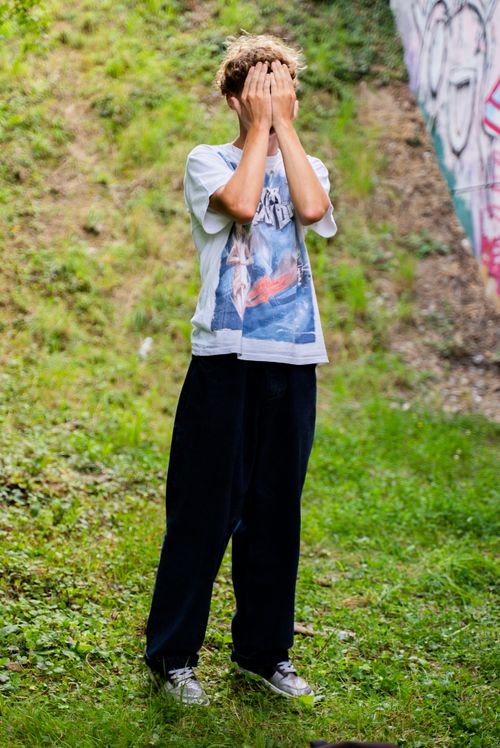 Free Person standing on grass outdoors with hands covering face, creating a mysterious vibe. Stock Photo