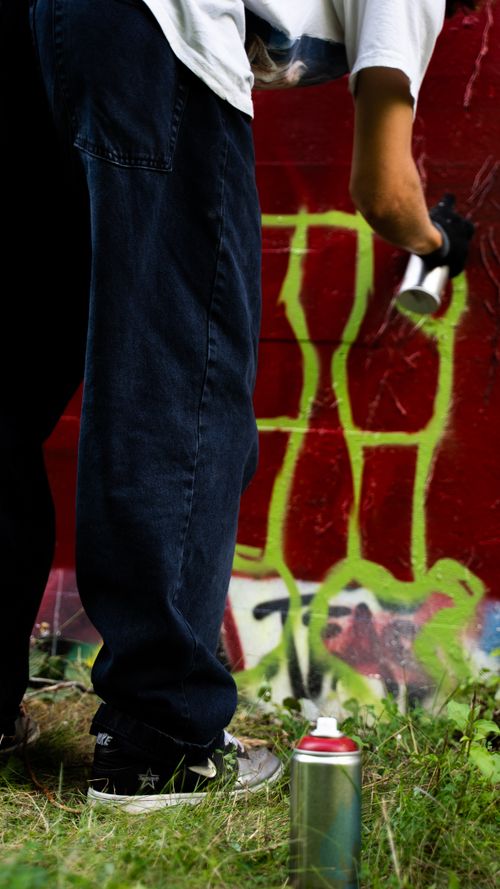 Free Unrecognizable artist spray painting graffiti on a wall outdoors. Stock Photo