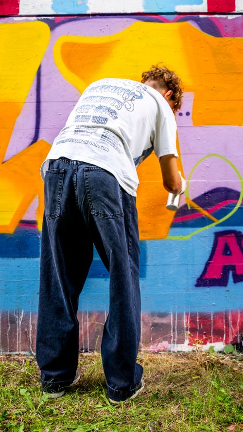Free Street artist spray painting a vibrant graffiti mural outdoors. Captured in a dynamic back view shot. Stock Photo